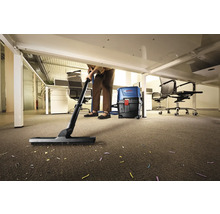 Eine Person reinigt mit einem Staubsauger einen Teppichboden im Büro unter einem Schreibtisch.