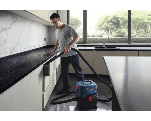 Ein Mann verwendet einen Nass Trockensauger von Bosch Professional in einer modernen Küche, um Staub zu entfernen.