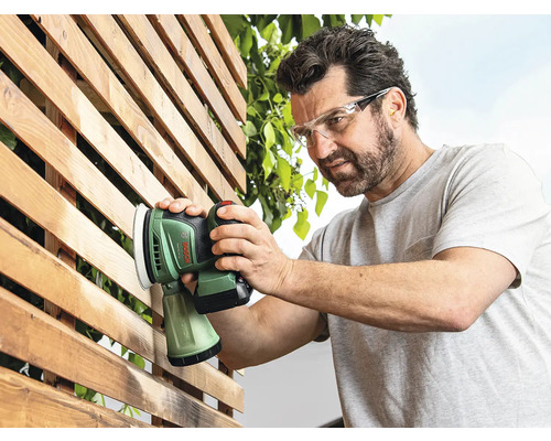 Mann schleift mit einem Exzenterschleifer eine Holzfläche im Außenbereich