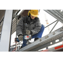 Handwerker beim Schneiden eines Werkstücks mit einem Akku-Winkelschleifer auf einem Gerüst.