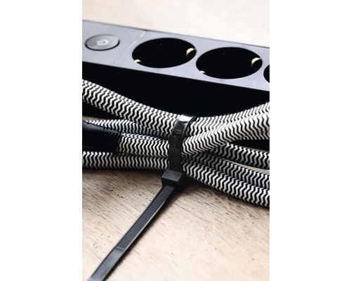 Eine Kabeltrommel mit Textilkabel und Kabelbinder liegt neben einer Steckdosenleiste.