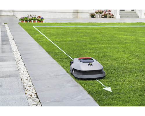 Rasenmähroboter auf Rasenfläche neben Gehweg mit Begrenzungskabel