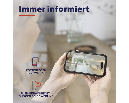 Eine Person hält ein Smartphone, das eine Küchenansicht zeigt und kostenlose Trust Wifi App und Push Benachrichtigungen bei Bewegung anzeigt.