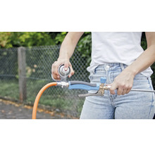 Eine Person sprüht ein Reinigungsmittel auf einen Wasserstrahlregler, der an einem Gartenschlauch befestigt ist.
