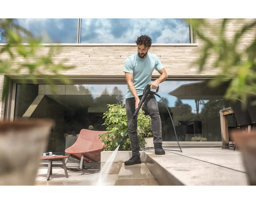 Mann reinigt Terrasse mit Hochdruckreiniger vor modernem Haus