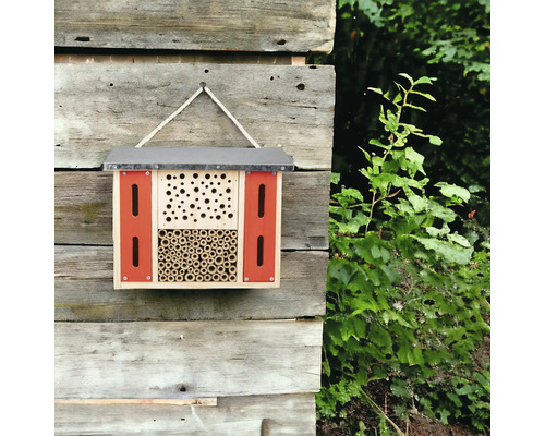 Insektenhotel aus Holz mit verschiedenen Füllmaterialien hängt an einer Holzwand.
