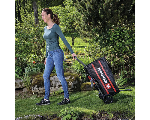 Frau zieht einen Einhell Gartenwagen durch einen Garten.