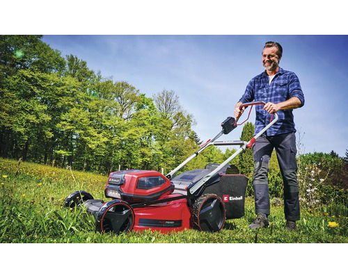 Mann mäht Rasen mit einem roten Akku-Rasenmäher von Einhell im Garten.