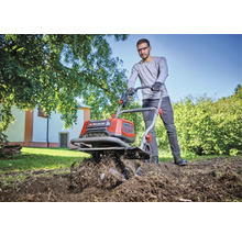 Ein Mann benutzt eine Motorhacke der Marke Einhell, um einen Garten umzugraben.