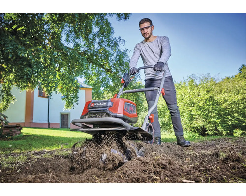 Ein Mann benutzt eine Motorhacke der Marke Einhell, um einen Garten umzugraben.