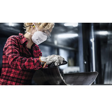 Eine Person mit Atemschutzmaske, Schutzbrille und Handschuhen bearbeitet ein Metallwerkstück.