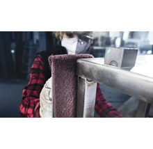 Eine Person reinigt eine Metallkonstruktion mit einem Schleifvlies.