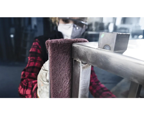 Eine Person reinigt eine Metallkonstruktion mit einem Schleifvlies.