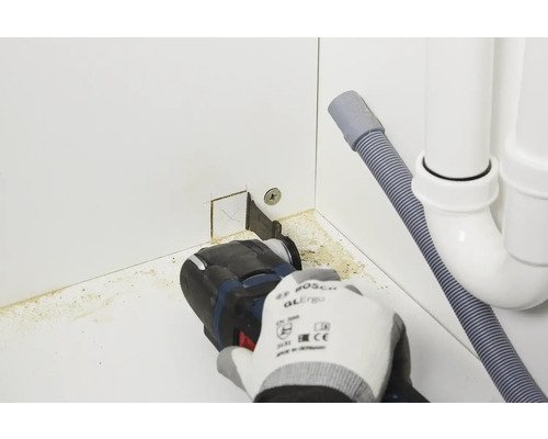 Eine Person verwendet ein Multifunktionswerkzeug zum Schneiden eines Schranks in der Nähe eines Abflusses.