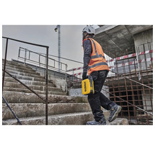 Ein Bauarbeiter mit Helm und Sicherheitsweste trägt eine gelbe Werkzeugkiste auf einer Baustelle die Treppe hoch.