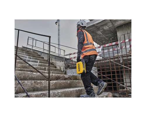 Ein Bauarbeiter mit Helm und Sicherheitsweste trägt eine gelbe Werkzeugkiste auf einer Baustelle die Treppe hoch.