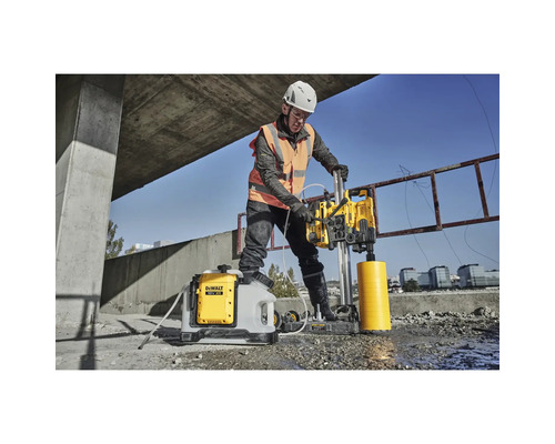 Ein Bauarbeiter bohrt mit einer Kernbohrmaschine ein Loch in Beton. Ein Wasserbehälter steht daneben.
