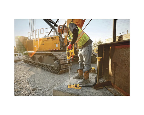 Ein Arbeiter bohrt mit einem Bohrhammer ein Loch in Beton, im Hintergrund ein Bagger
