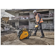 Ein Bauarbeiter bedient eine gelbe Rüttelplatte auf einer Baustelle.