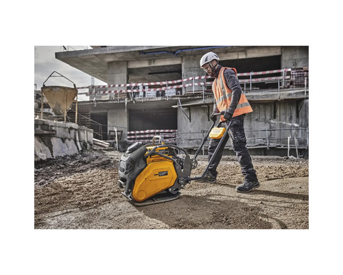 Ein Bauarbeiter bedient eine gelbe Rüttelplatte auf einer Baustelle.