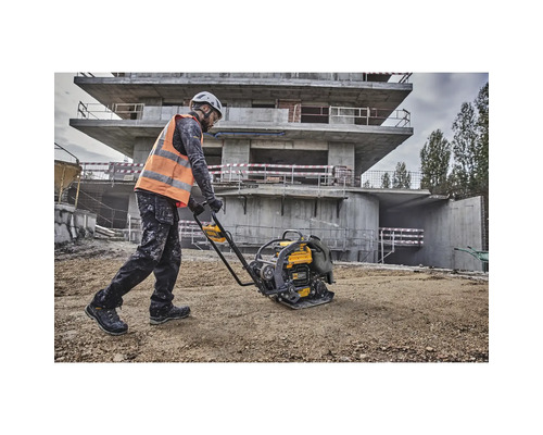 Ein Bauarbeiter verdichtet mit einer Rüttelplatte den Boden auf einer Baustelle.