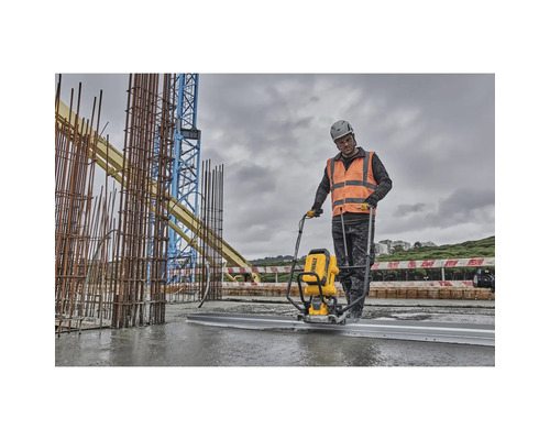 Ein Bauarbeiter verwendet eine Betonabziehmaschine auf einer Baustelle, im Hintergrund befinden sich Baustahl und ein Kran.