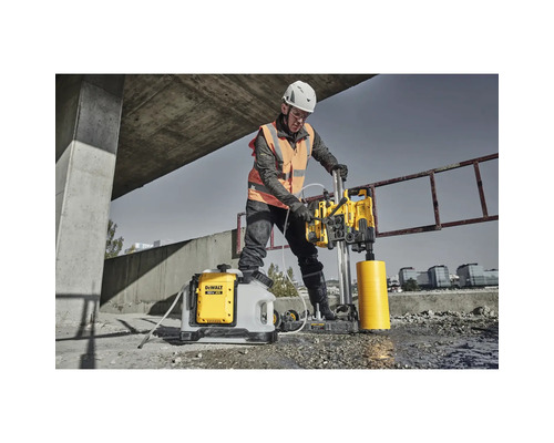 Bauarbeiter bedient eine DeWalt Kernbohrmaschine mit Wasserbehälter auf einer Baustelle.
