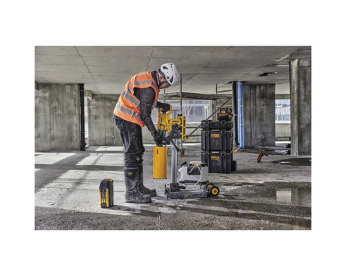 Ein Bauarbeiter bedient eine Kernbohrmaschine auf einer Baustelle. Im Hintergrund sind Werkzeugkisten zu sehen.