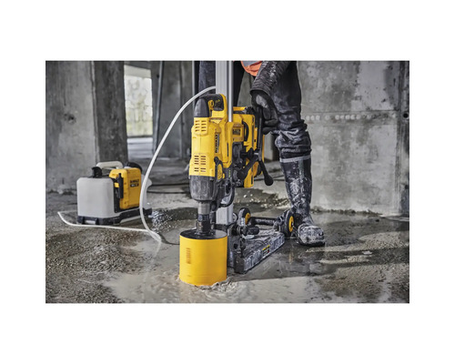 Bediener verwendet eine gelbe DeWalt Kernbohrmaschine zum Bohren eines Lochs in einen Betonboden. Eine Wasserpumpe befindet sich im Hintergrund.