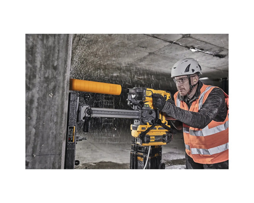 Ein Arbeiter bohrt mit einer gelben Bohrmaschine ein Loch in eine Betonwand, während Wasser spritzt.