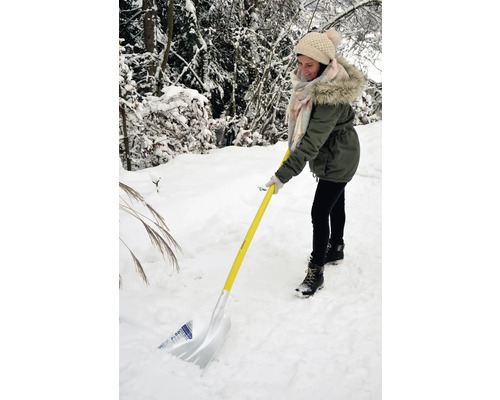 Frau schippt Schnee mit einer Schneeschaufel mit gelbem Griff im Winter