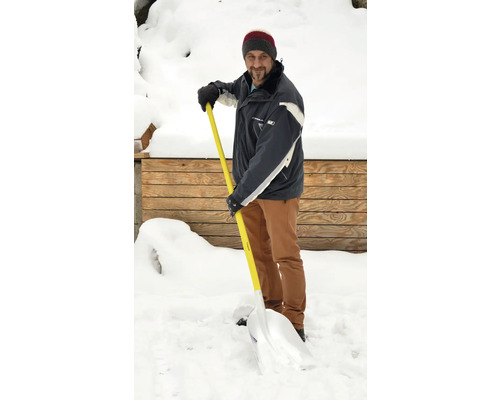 Mann schaufelt Schnee mit einer Schneeschaufel vor einem Holzhaus