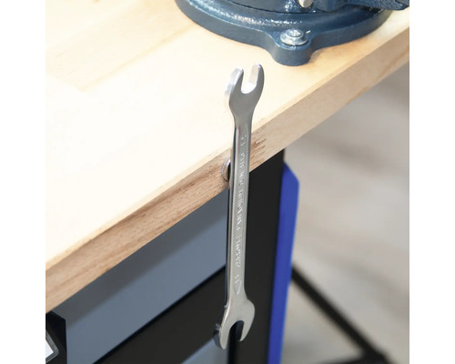 Ein offener Ringschlüssel hängt an einer Werkbank.