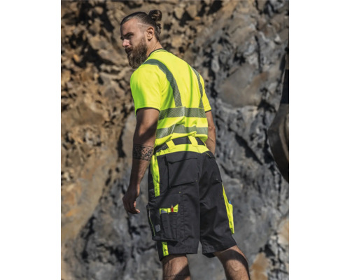 Mann trägt Warnschutzkleidung mit T-Shirt und Shorts vor felsigem Hintergrund