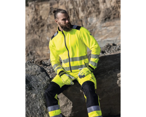 Mann in Warnschutzkleidung sitzt auf einem Felsen.