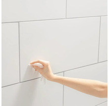Eine Hand reinigt eine weiße geflieste Wand mit einem Tuch.