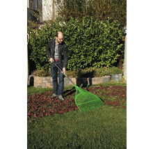 Mann harkt Blätter mit einem Laubbesen im Garten.