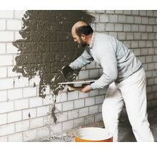 Mann trägt Putz auf eine Ziegelwand auf