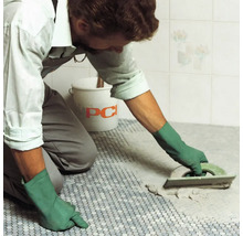 Ein Handwerker verfugt Mosaikfliesen mit einem Fugenbrett, ein Eimer der Firma PCI steht im Hintergrund.