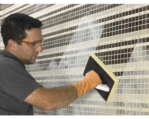 Eine Person verfugt Mosaikfliesen mit einem Fugbrett.