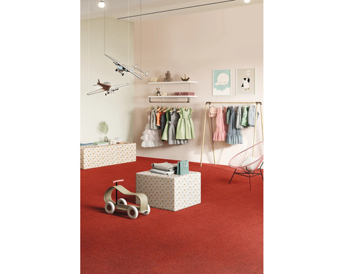 Kinderbekleidungsgeschäft mit Kleidern, Spielzeugflugzeugen und Holzspielzeug auf rotem Teppich.