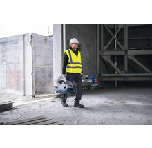 Ein Bauarbeiter mit Schutzhelm und Warnweste trägt eine Bosch Metallsäge auf einer Baustelle.