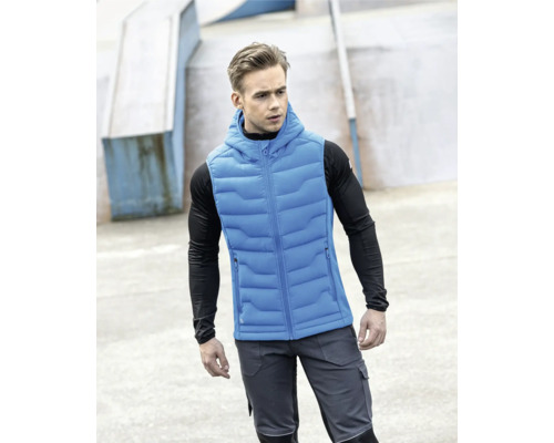 Mann trägt eine blaue Steppweste mit Kapuze über einem schwarzen Langarmshirt und graue Arbeitshosen.