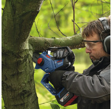 Ein Mann schneidet mit einer Akku-Kettensäge einen Ast.