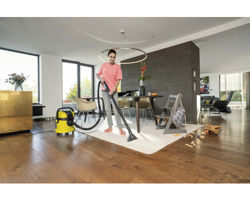 Frau reinigt Teppich mit einem Waschsauger in einem Wohnzimmer