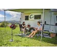 Szene mit Wohnmobil, Markise, Tisch, Stühlen und Personen auf einer Wiese.