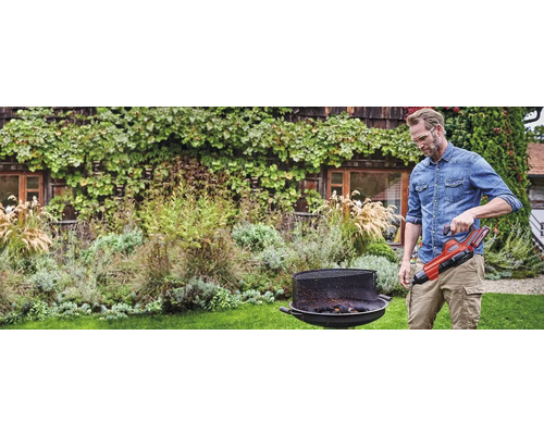 Mann zündet Grill mit Anzündkamin im Garten an