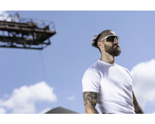 Ein Mann mit Bart und Sonnenbrille vor blauem Himmel