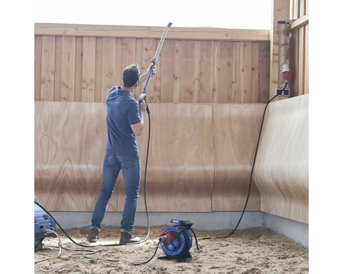 Mann benutzt einen Hochdruckreiniger in einem Raum mit Holzwänden und einem Stromkabelaufroller