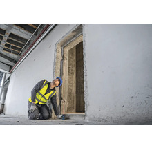 Ein Bauarbeiter mit Schutzhelm und Sicherheitsweste misst eine Türöffnung mit einem Laser Entfernungsmesser.